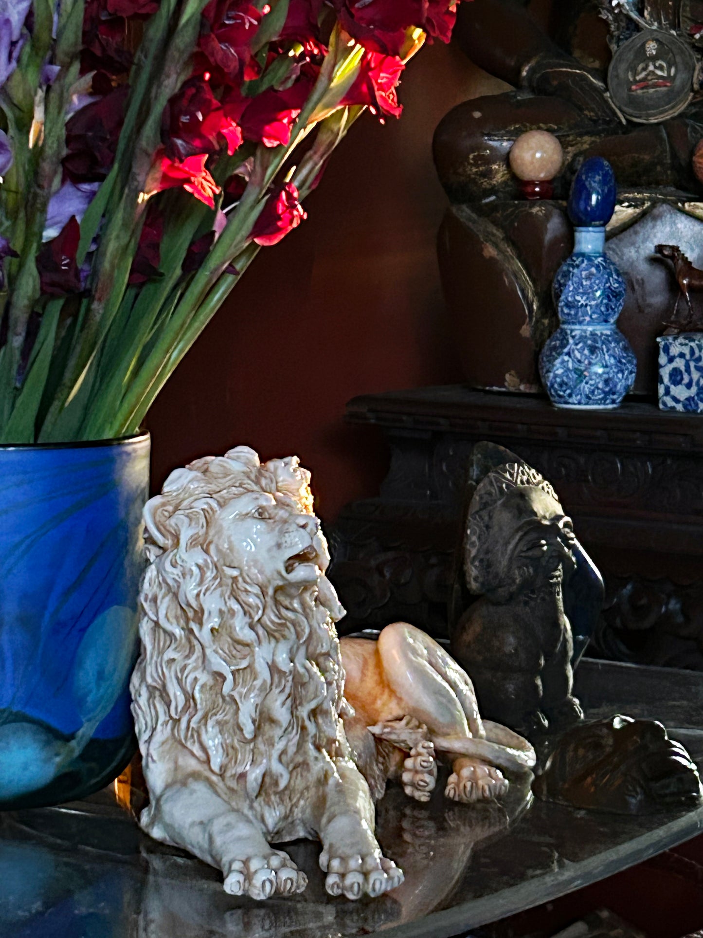 Porcelain lion displayed in an interior setting beside a vase of gladioli for scale