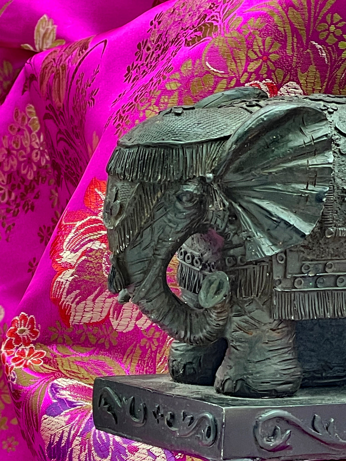 Front view of elephant head with tasselled headdress and curled trunk