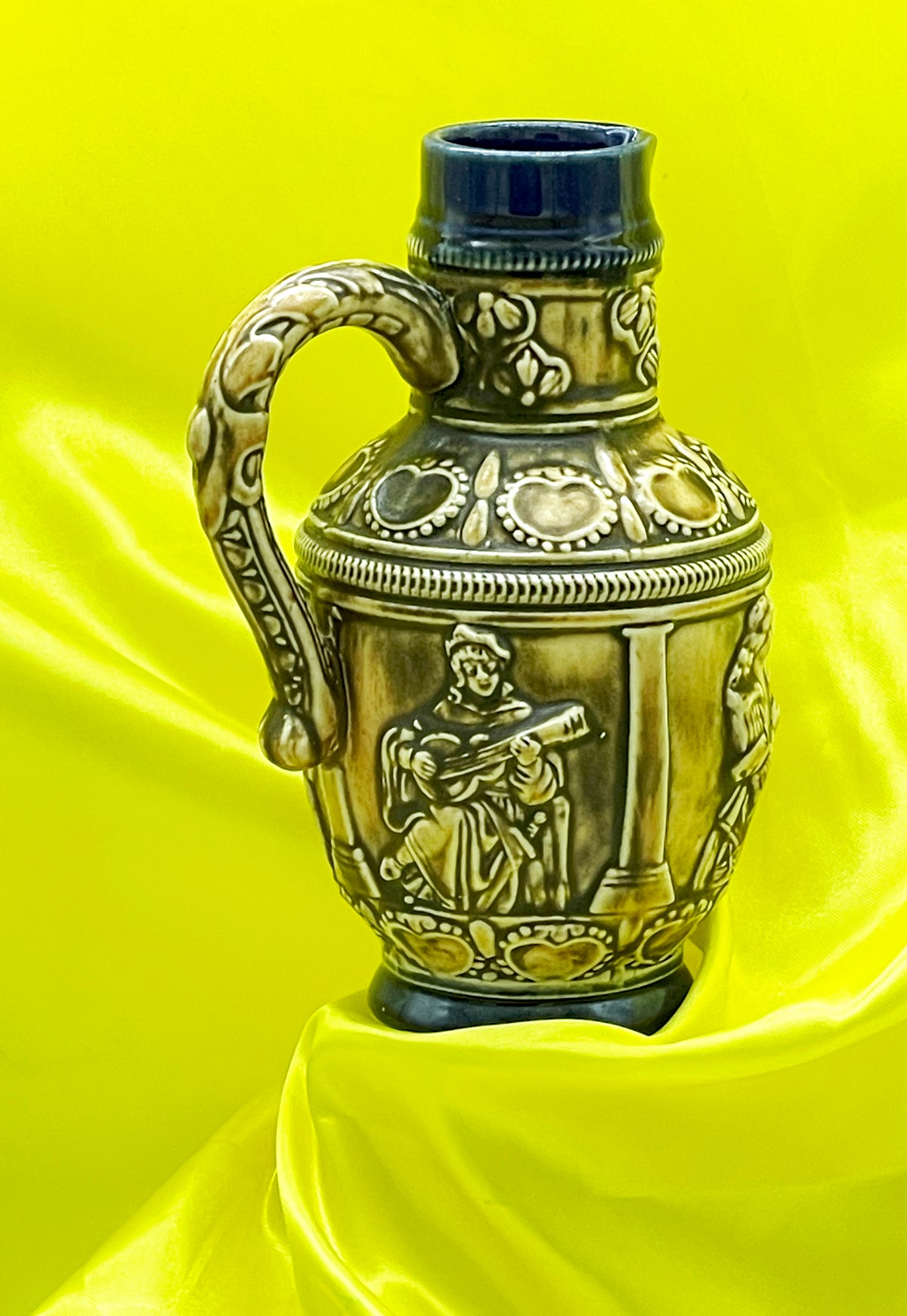 Vintage West German ceramic jug with musician relief, ivory glaze and cobalt blue rim, front view