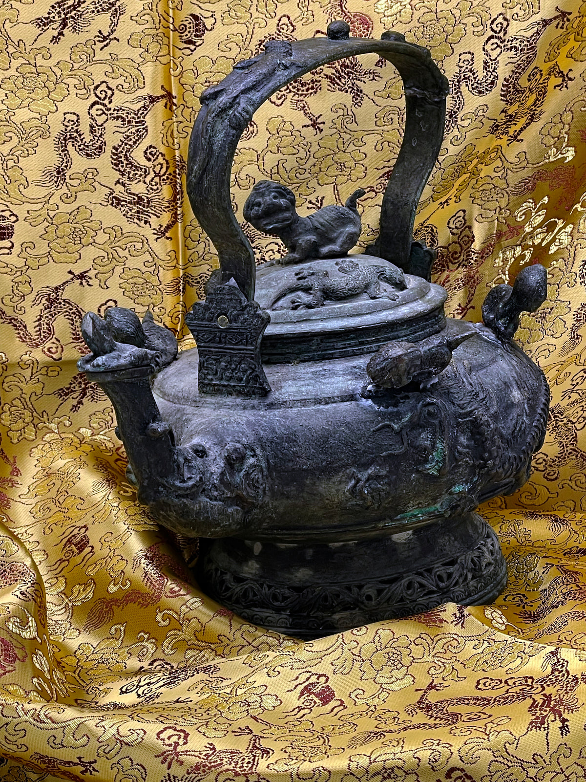 Antique Chinese bronze ritual teapot with mythical creatures and green patina on golden dragon silk, front view