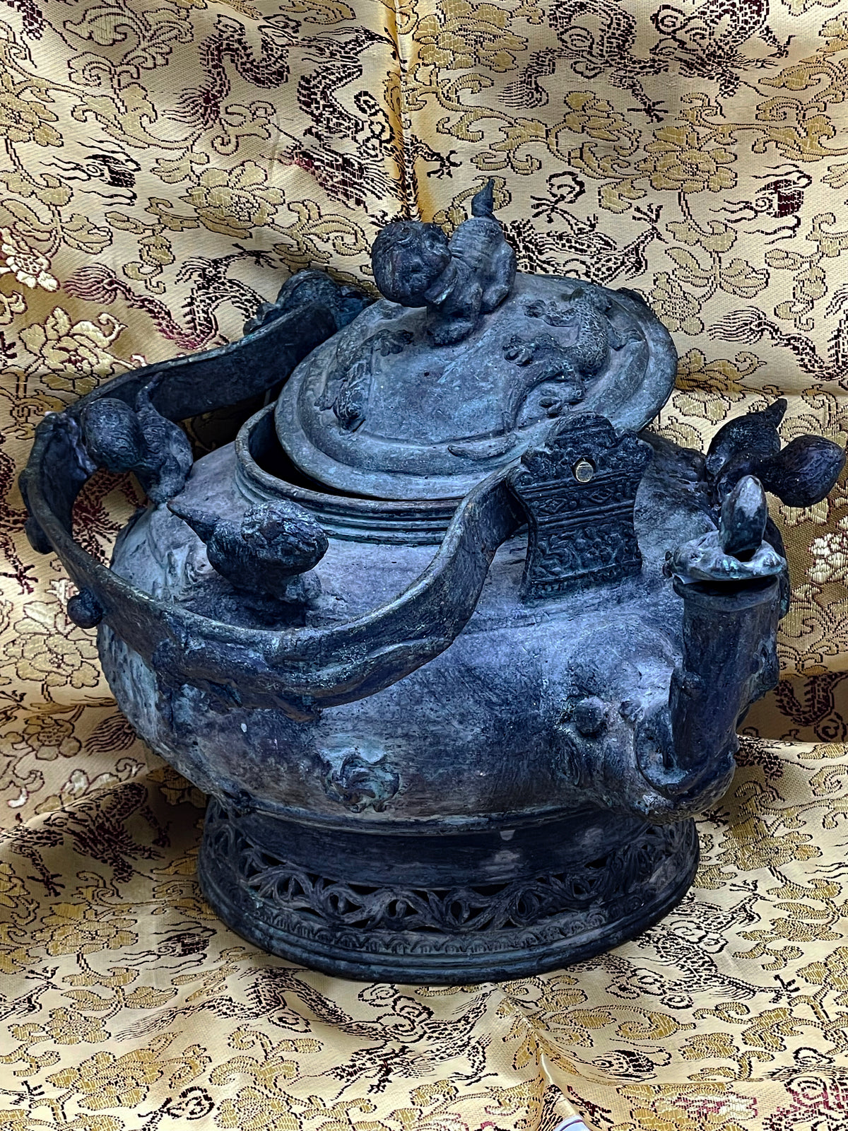 Top angle of Chinese bronze teapot with lid slightly open showing qilin relief and shoulder creatures
