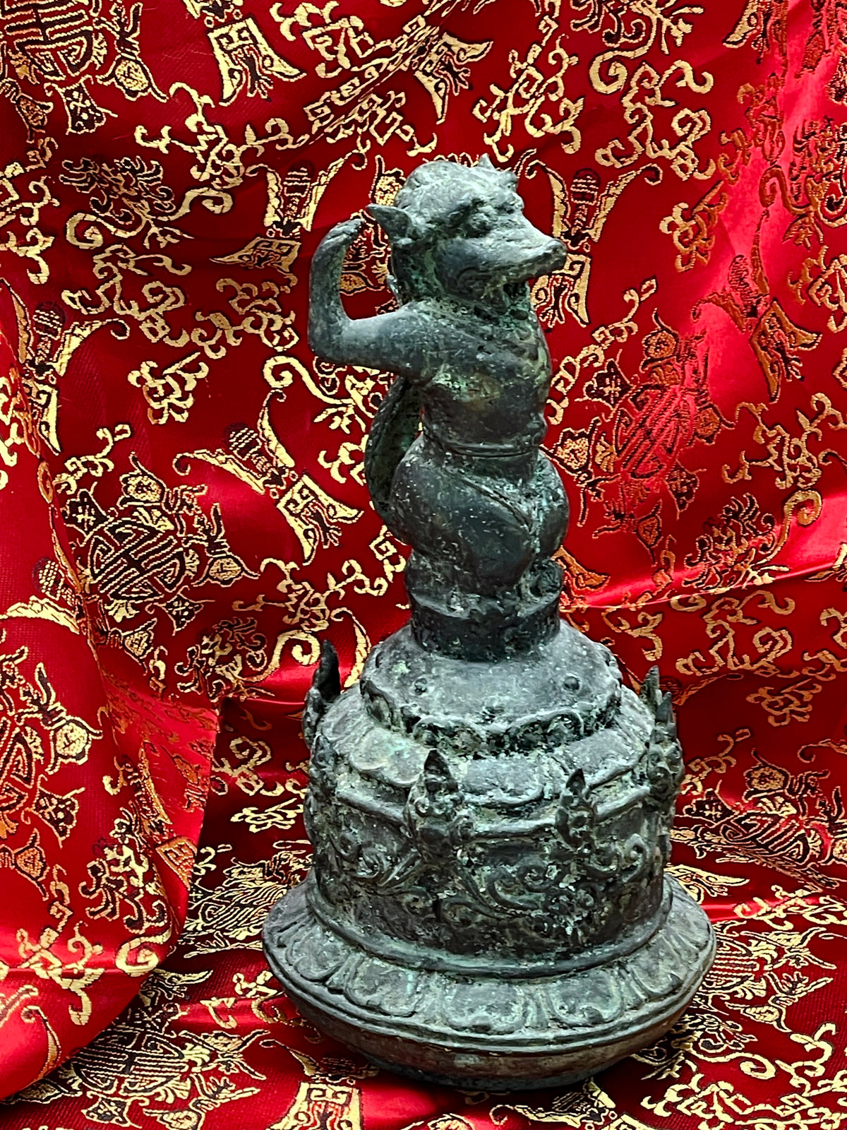 Antique Chinese bronze ritual bell with mythical monkey guardian figure, front view on red silk
