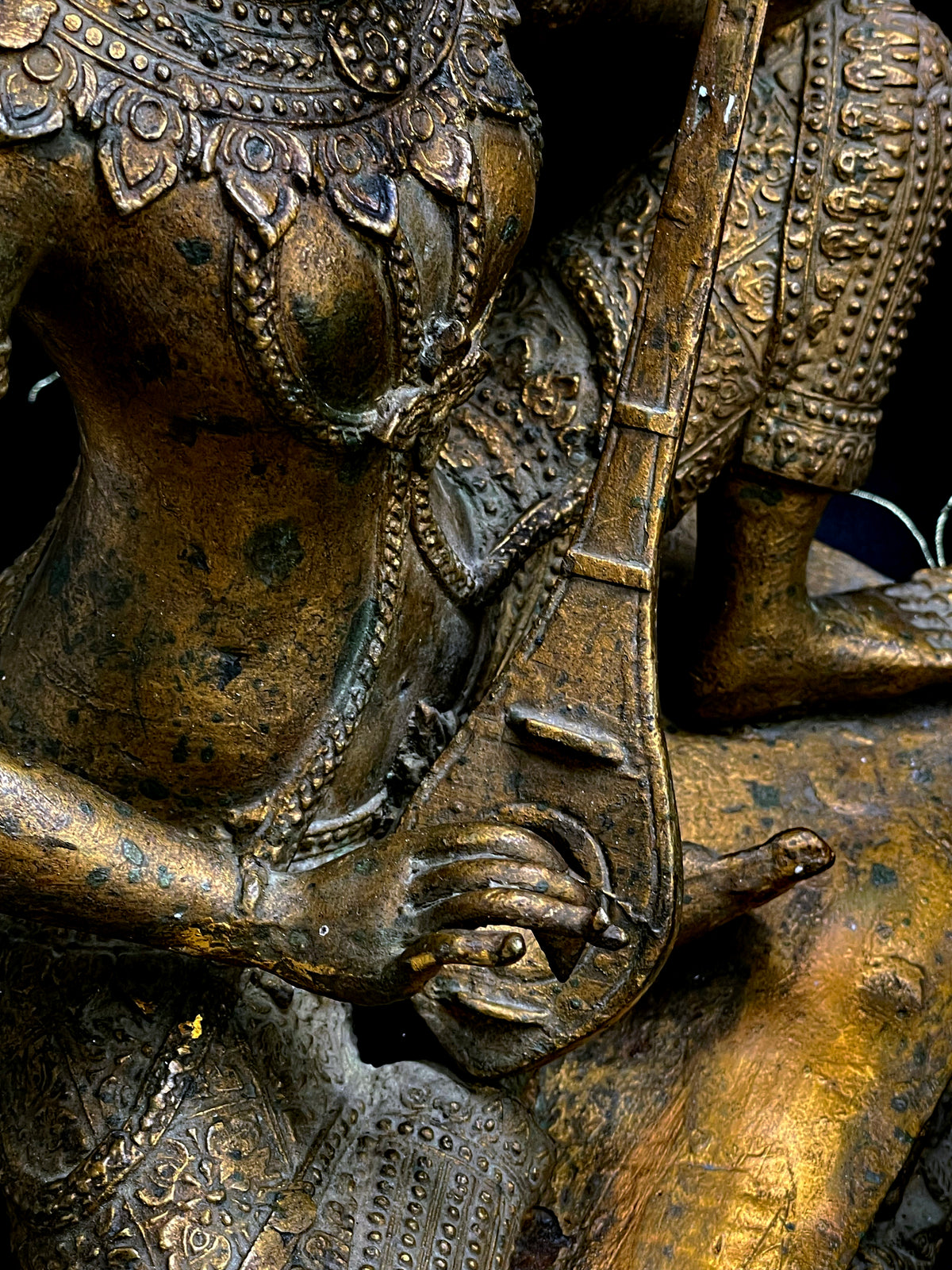 Detail of Saraswati's finely cast hand plucking the strings of the vina soundbox
