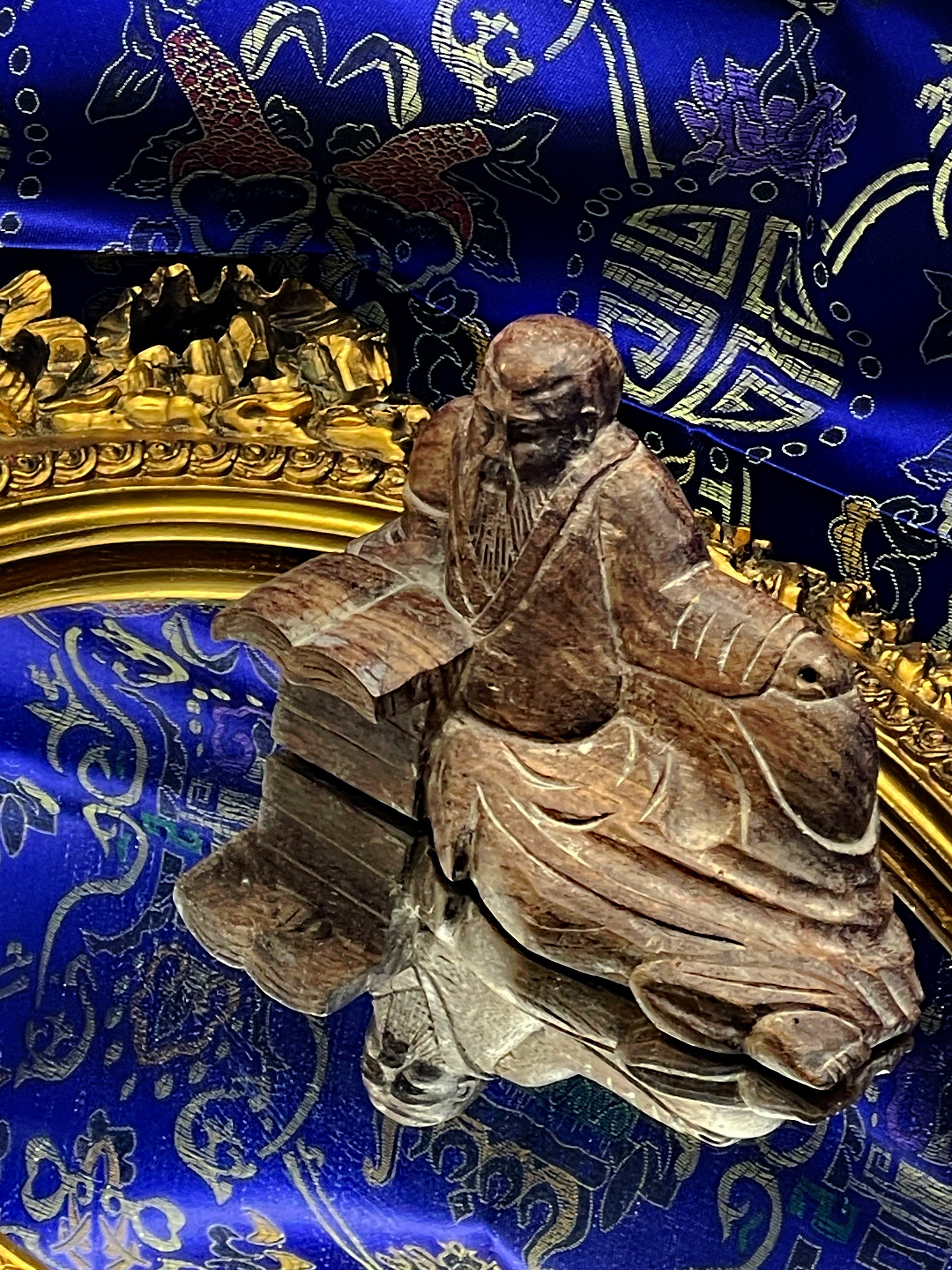 Confucius figure resting against the ornate gilded mirror frame