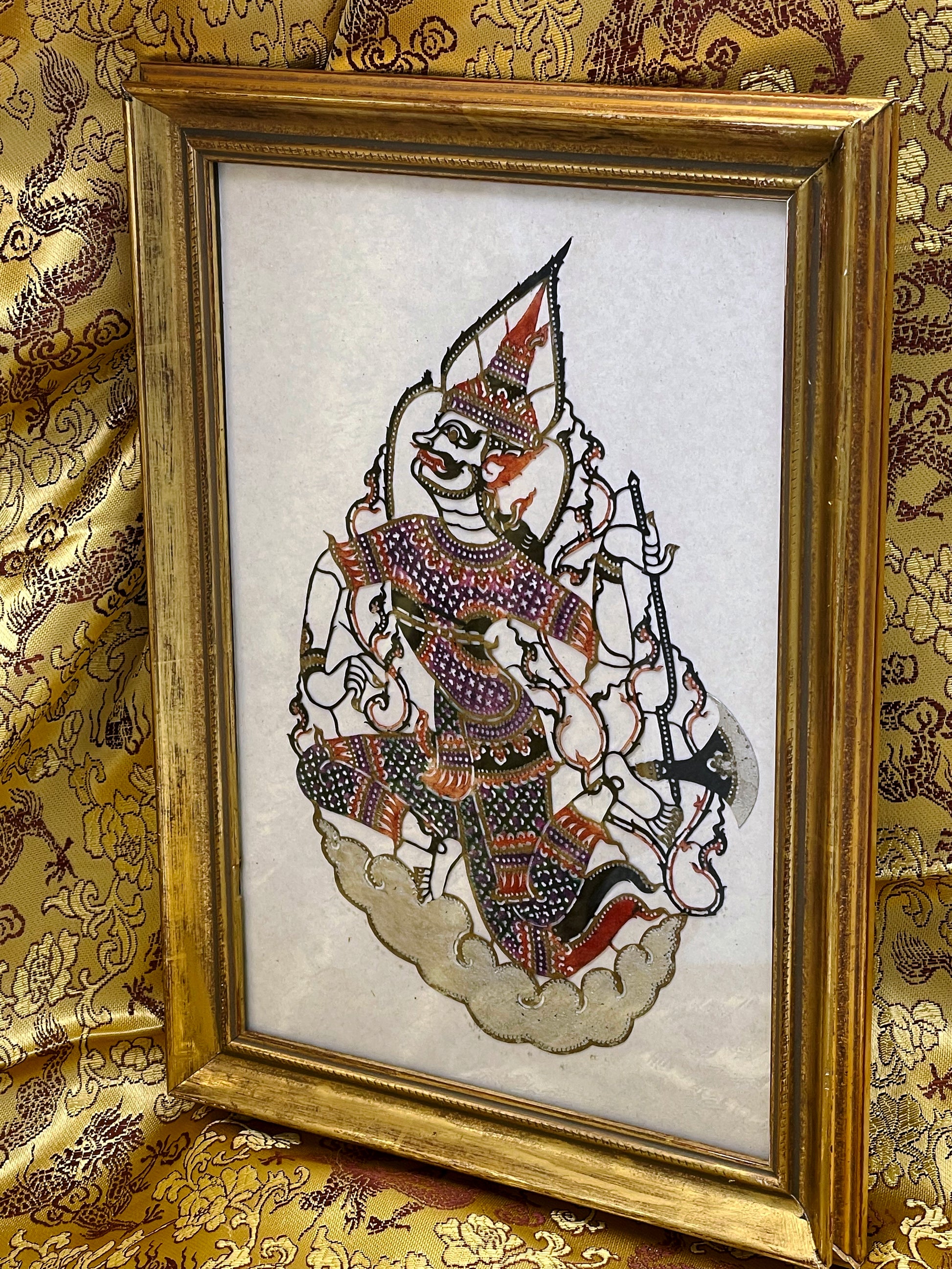 Indonesian hand-coloured pierced leather deity in a gilded vintage frame under glass