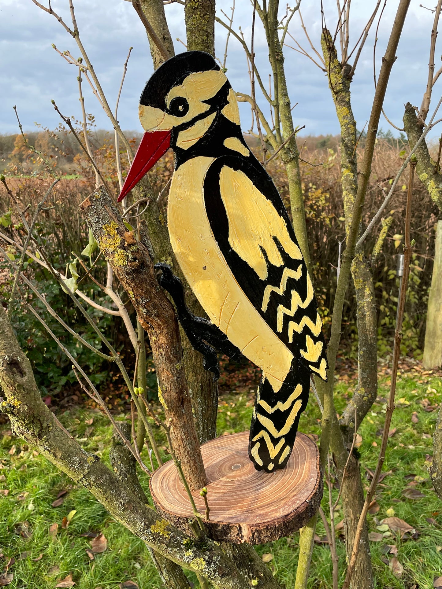 Wooden woodpecker sculpture perched on branch and round log base showing scale