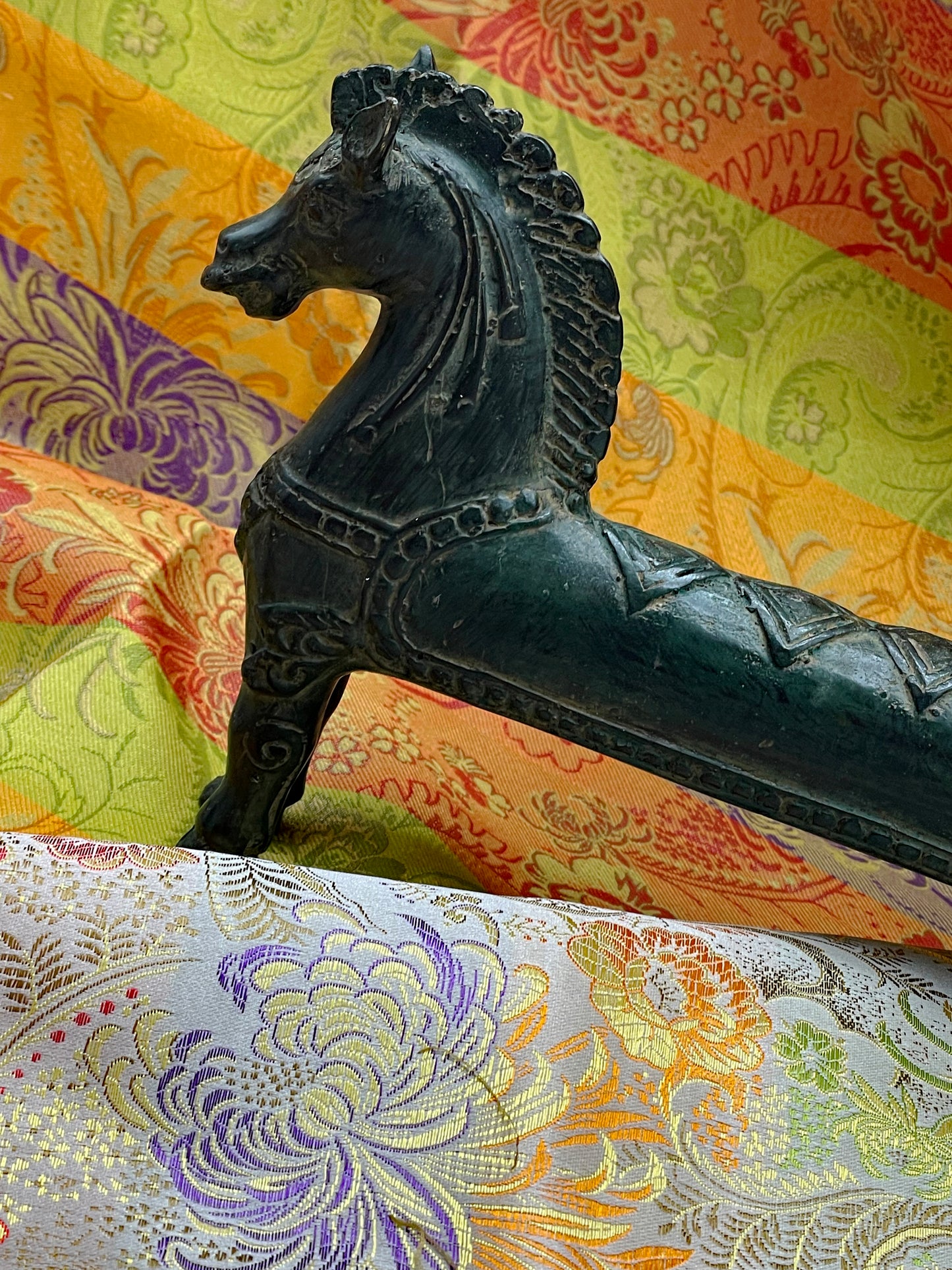 Side profile of the long bronze horse with curled tail and incised saddle blanket