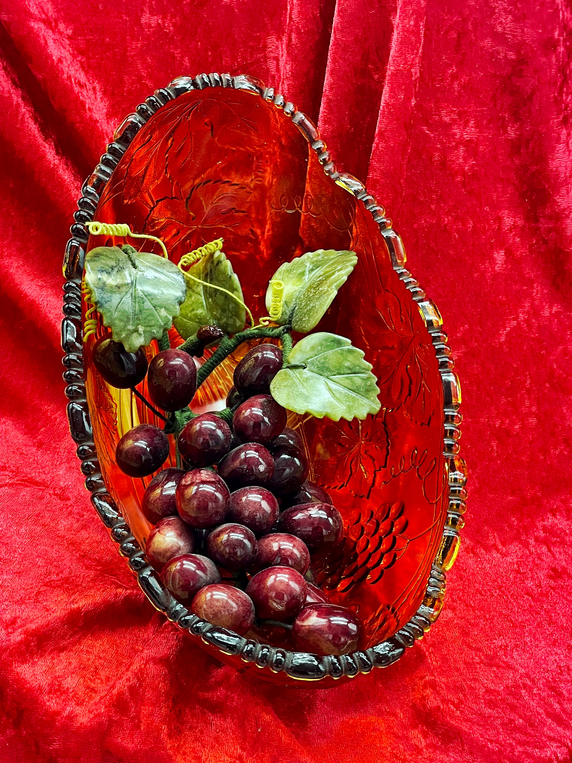 Top-down view of the oval amber glass bowl filled with amethyst grapes and jade leaves