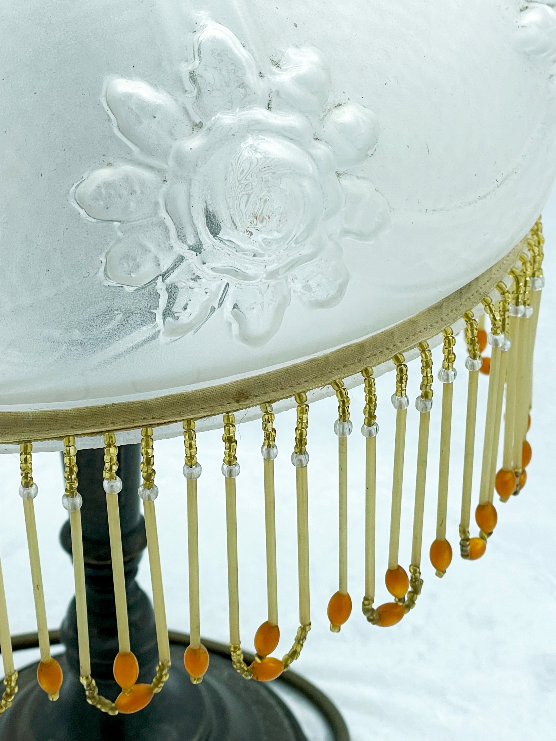 Close detail of relief moulded rose on the frosted glass shade above the beaded fringe