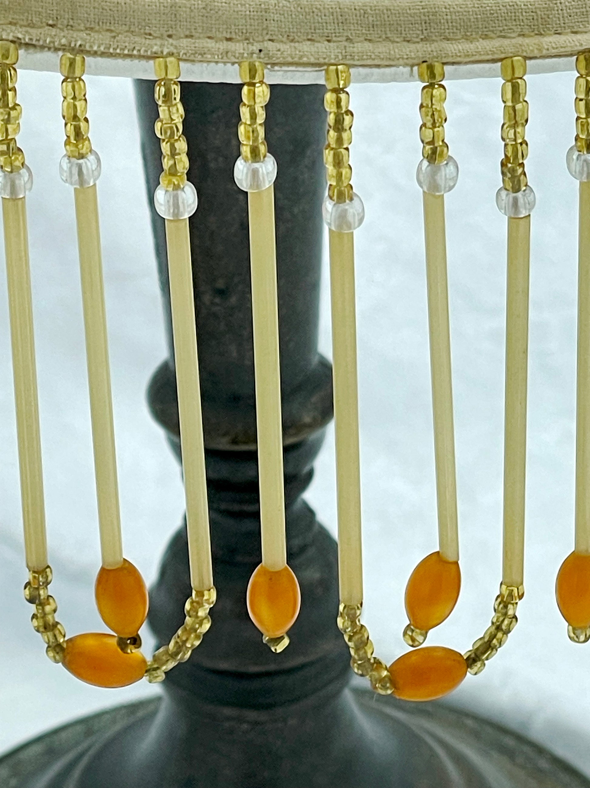 Beaded fringe draped over the dark cast metal stem of the lamp