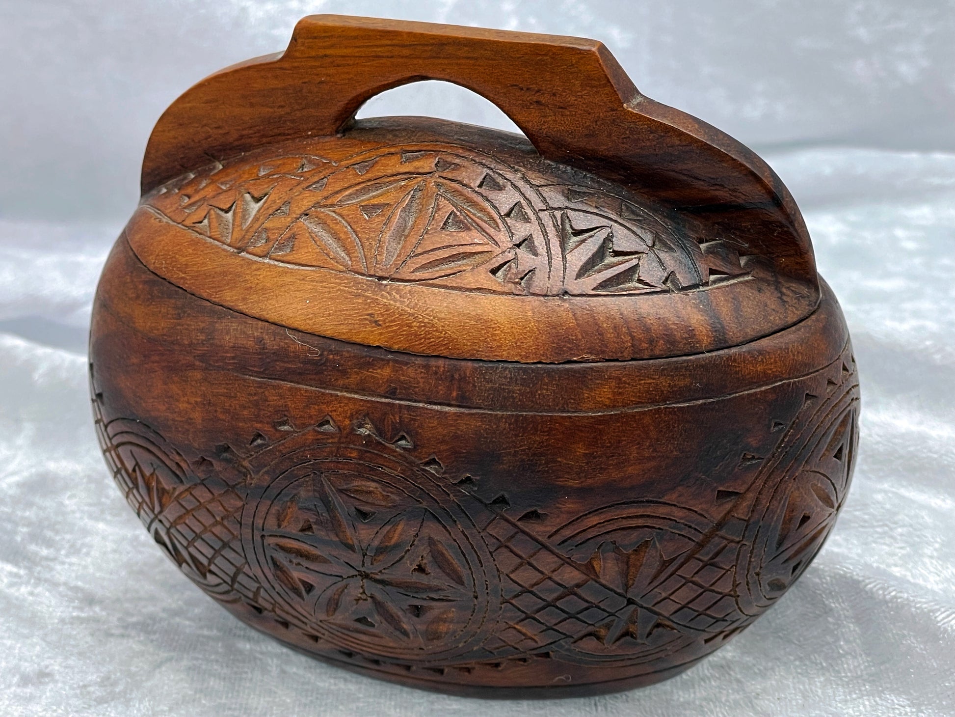 Oval hand-carved dark hardwood lidded box with chip-carved folk art lid and arched handle, closed three-quarter view