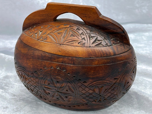 Oval hand-carved dark hardwood lidded box with chip-carved folk art lid and arched handle, closed three-quarter view