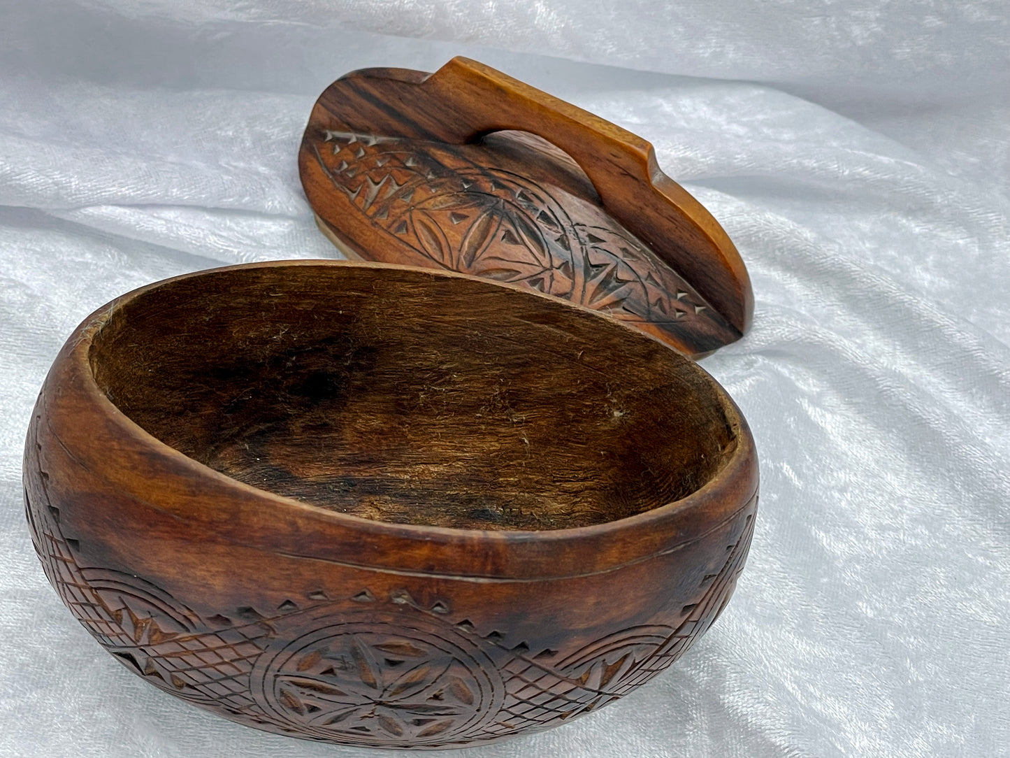 Wooden box opened with lid removed, revealing the smooth oval interior and chip-carved base