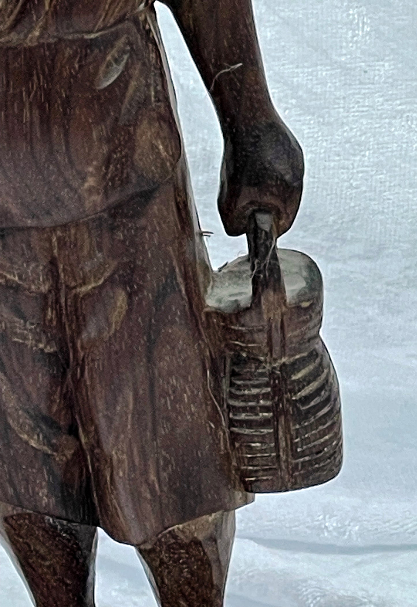 Detail of the carved hand holding a woven creel lantern on the hardwood figure