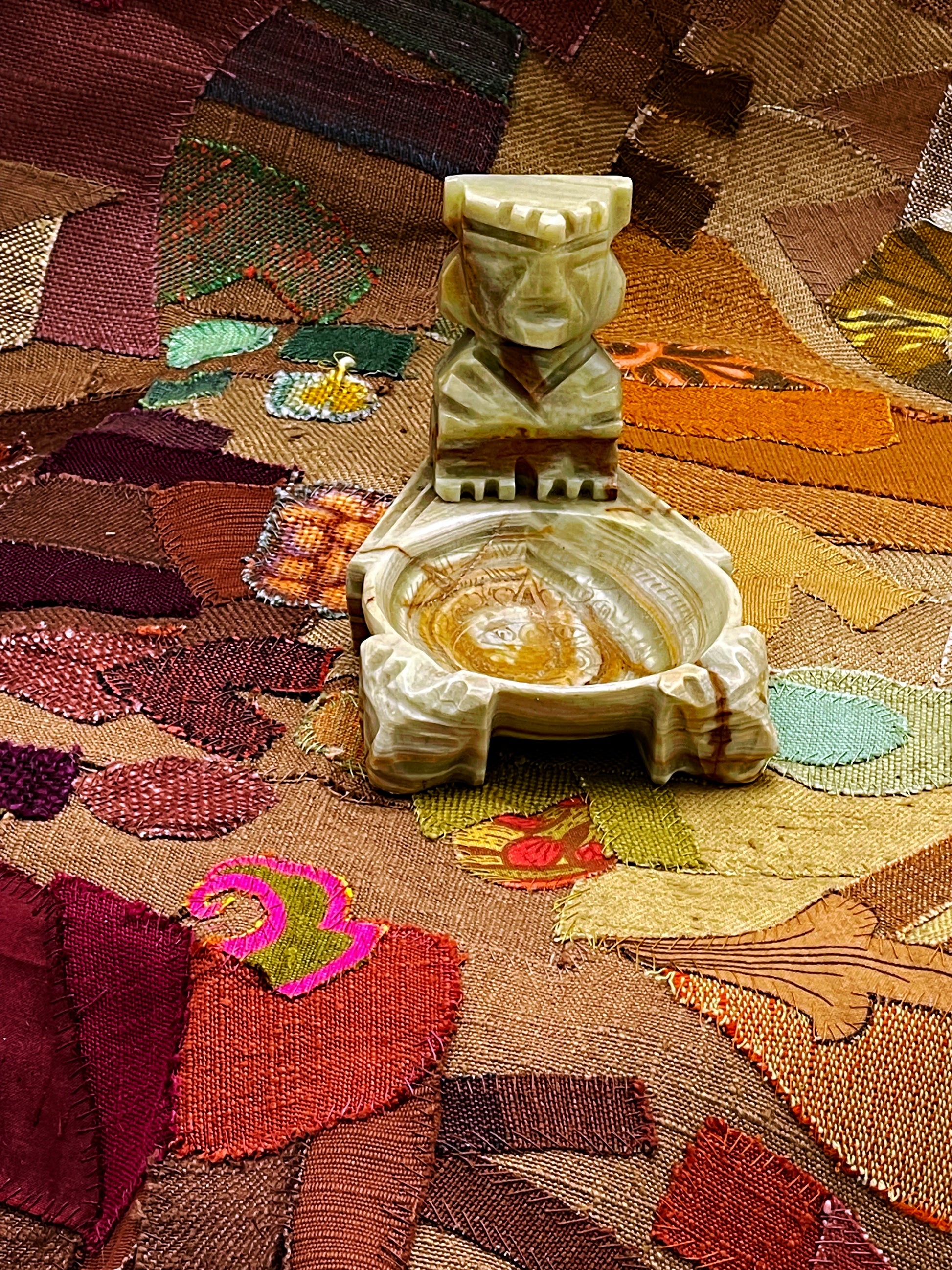 Hand-carved green onyx Aztec smoking dish standing on patterned textile, full view
