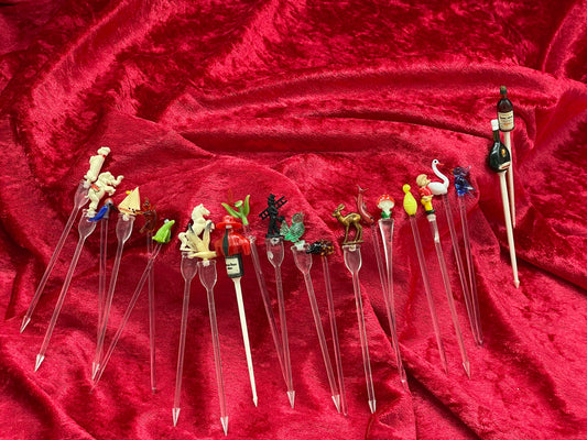 Full fanned array of vintage figural cocktail picks on red velvet, glass and celluloid toppers
