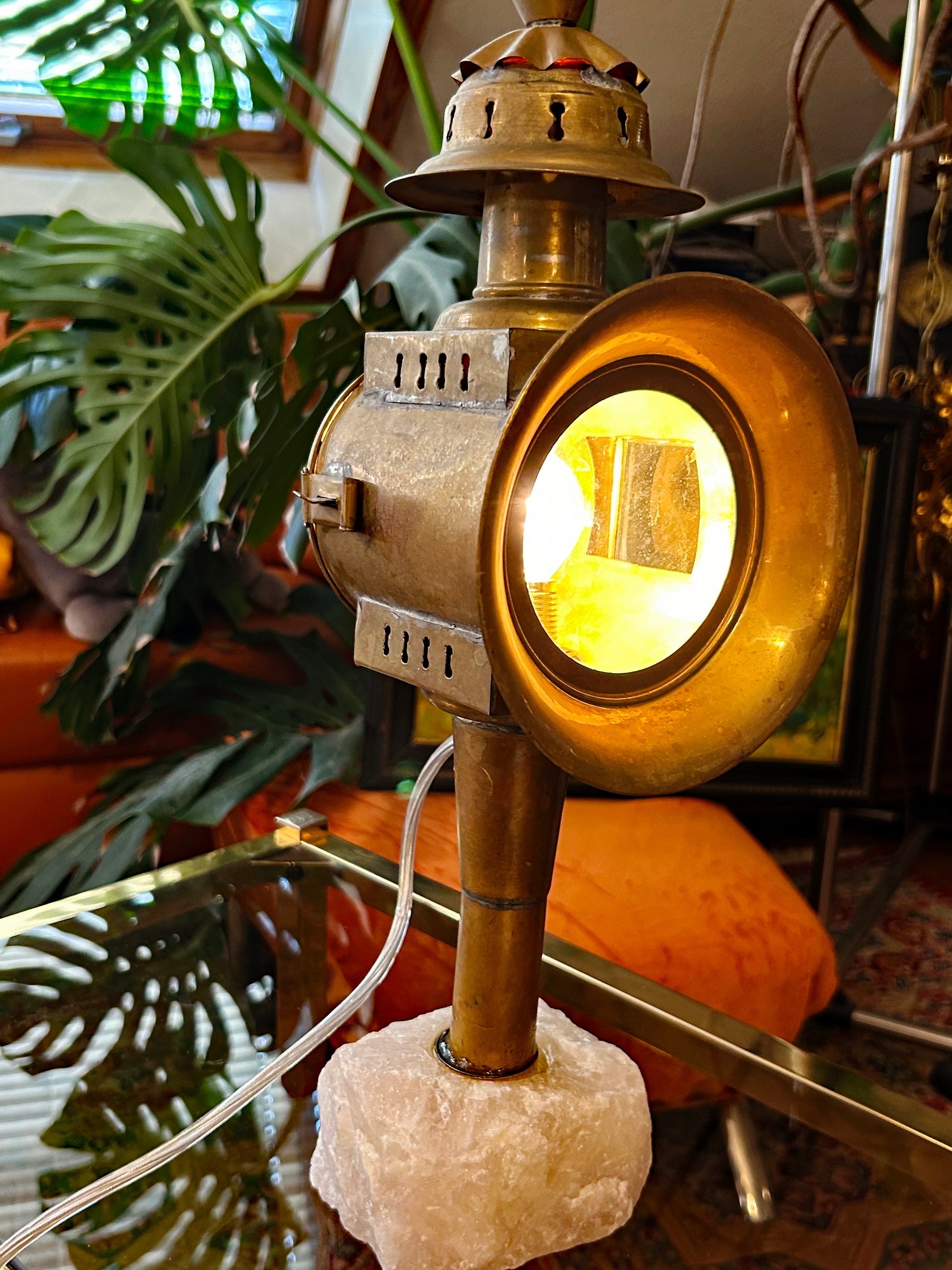 Antique coach lantern with glowing round beveled lens on raw rose quartz crystal base