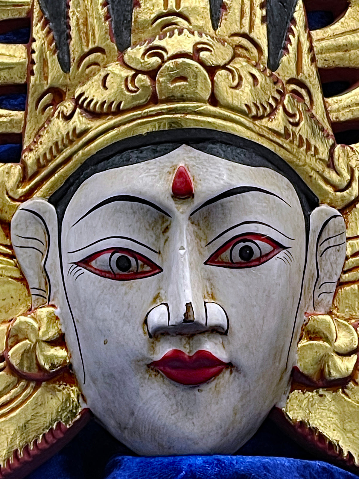 Detail view of the hand-carved Balinese theatre wall mask showing gilding and carving work