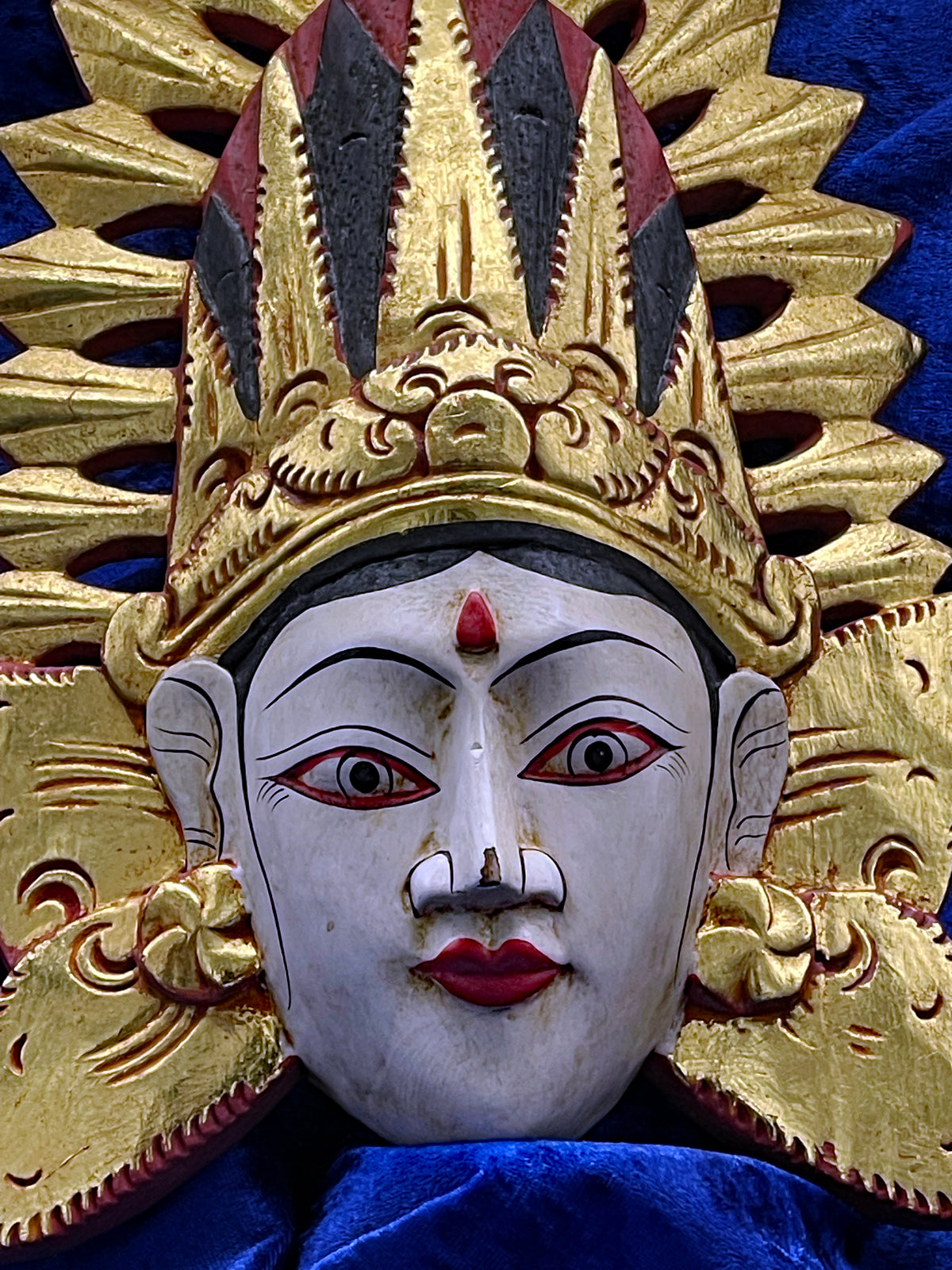 Close-up of the serene white painted face of the Balinese theatre mask with red lips and bindi