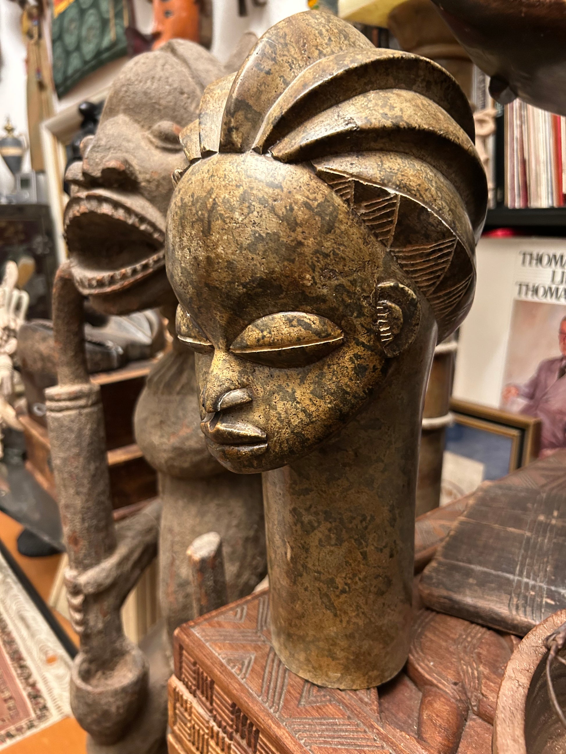 Large Benin-style hand-carved stone head sculpture, three-quarter view showing serene face and braided crown