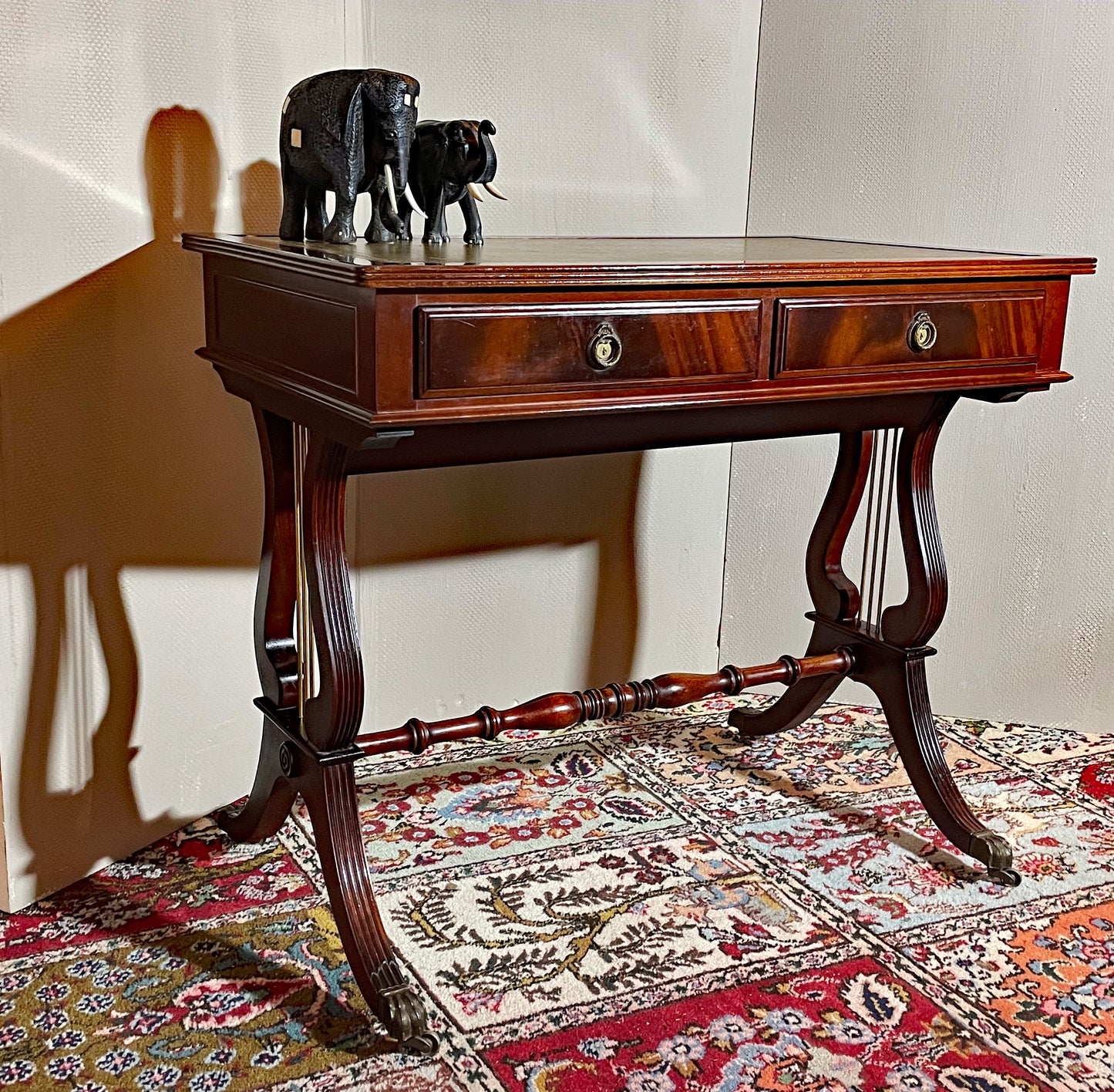 Regency-style mahogany lyre-end console table with green leather top and brass castors, three-quarter view