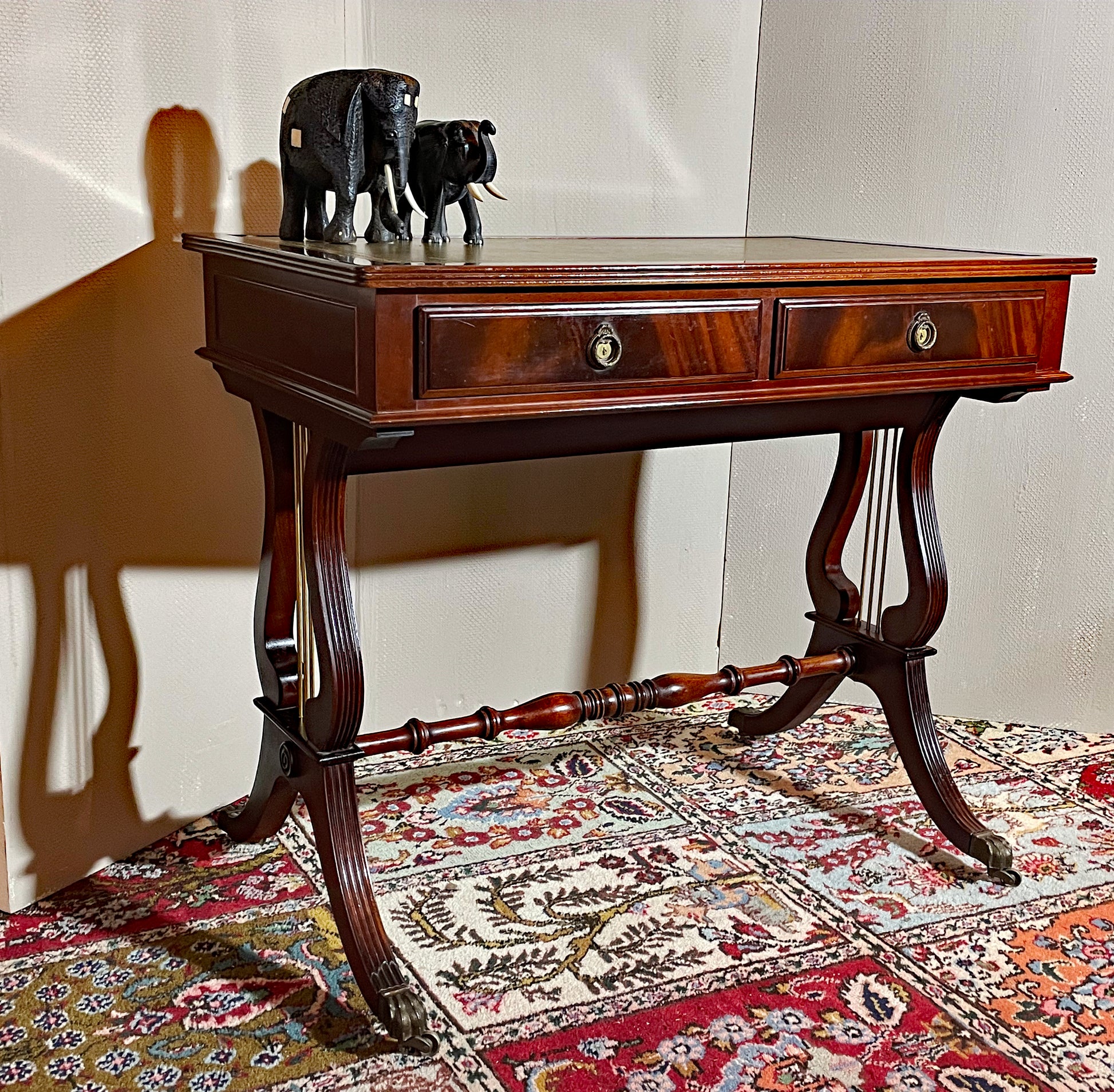 Regency-style mahogany lyre-end console table with green leather top and brass castors, three-quarter view