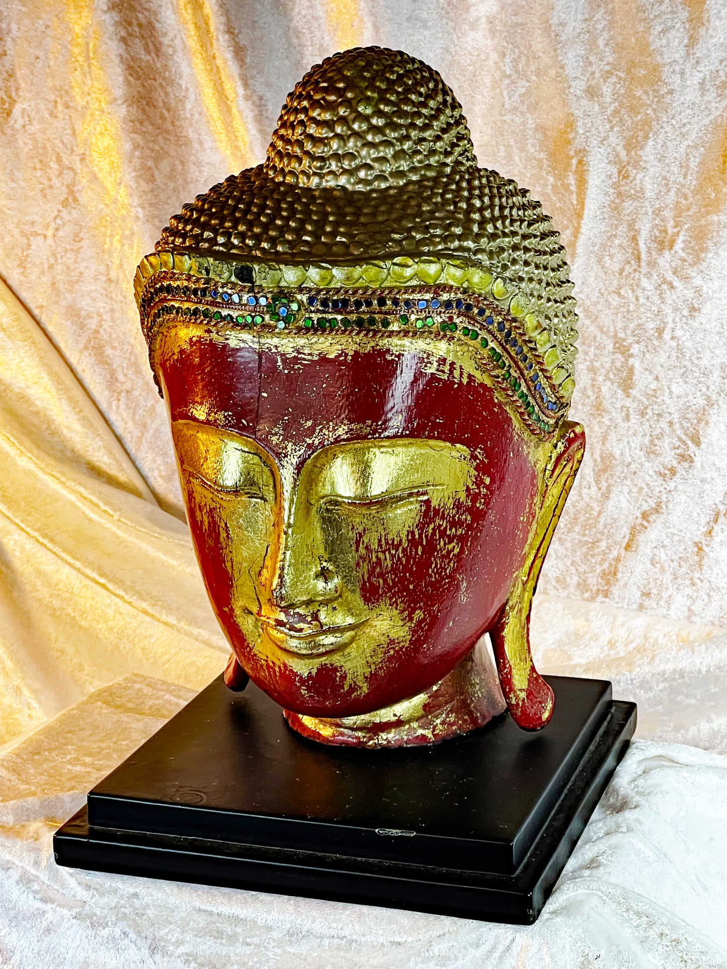Red lacquer and gilded Buddha head, three-quarter view against warm gold backdrop