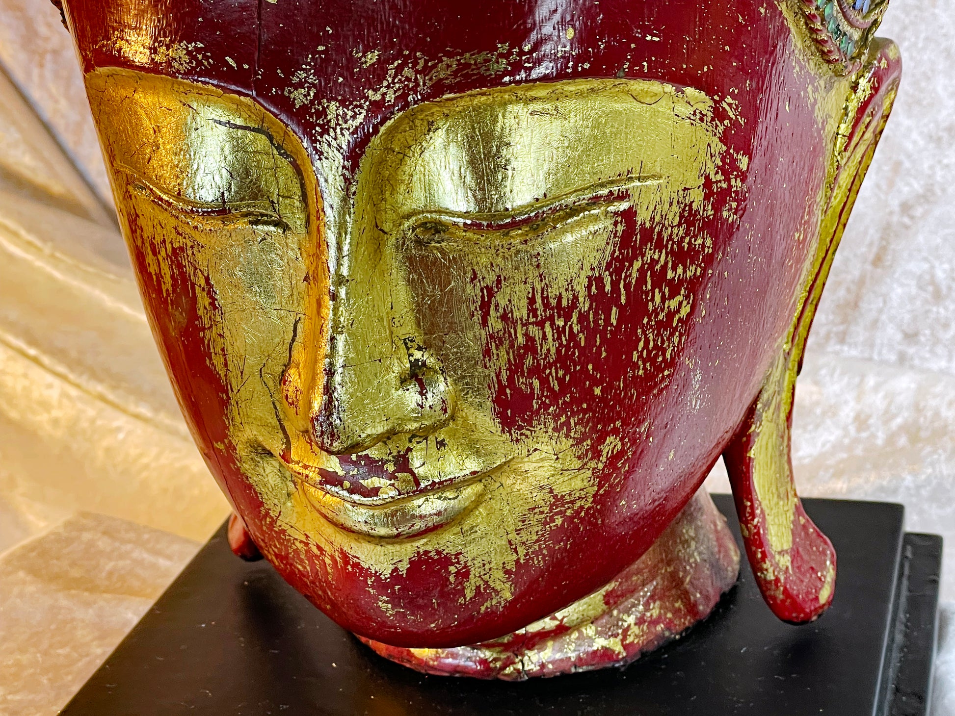 Detail of the Buddha's face showing worn gold leaf over deep red lacquer