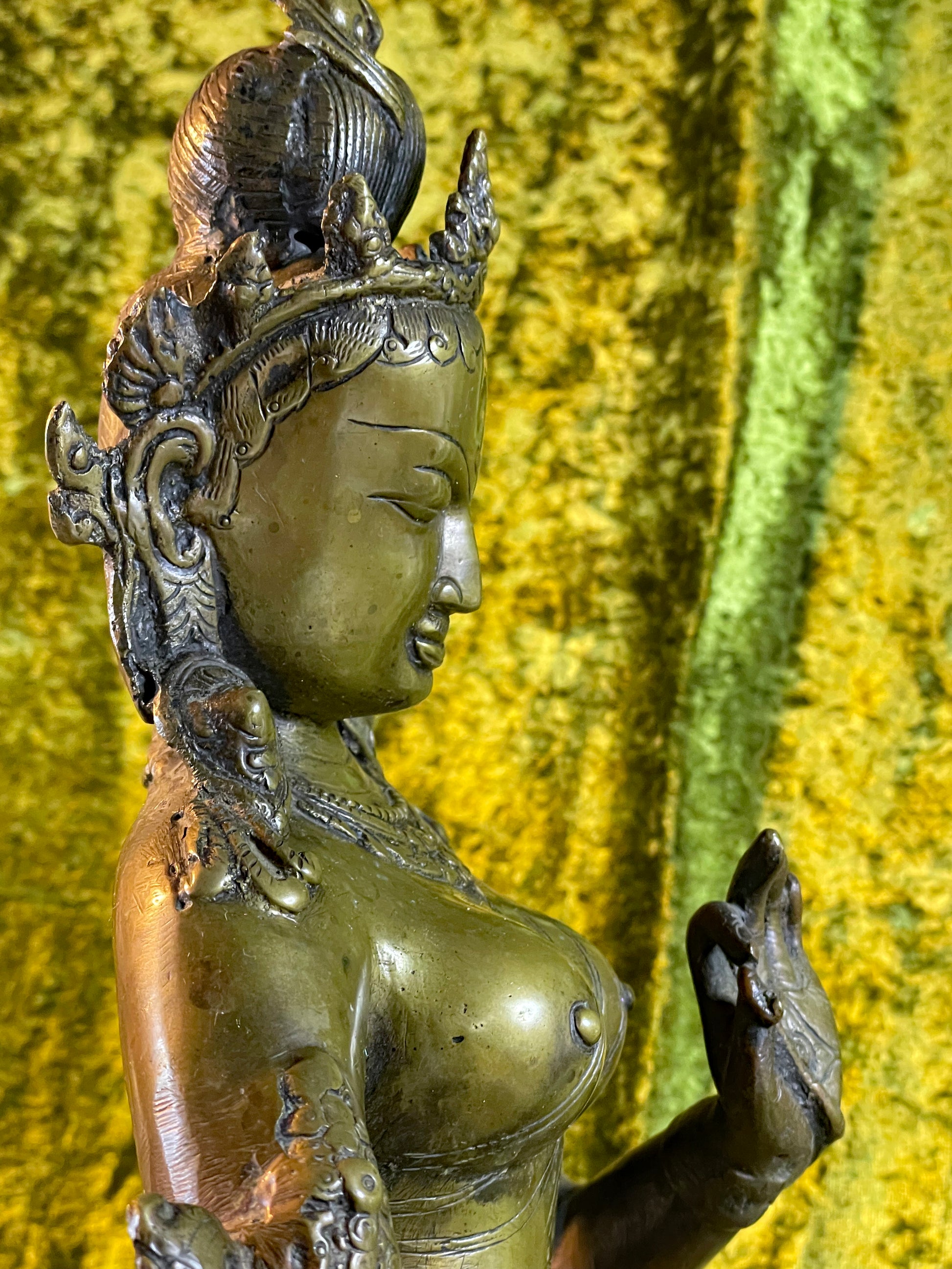 Detail of the figure's torso, beaded necklaces and raised left hand holding a lotus