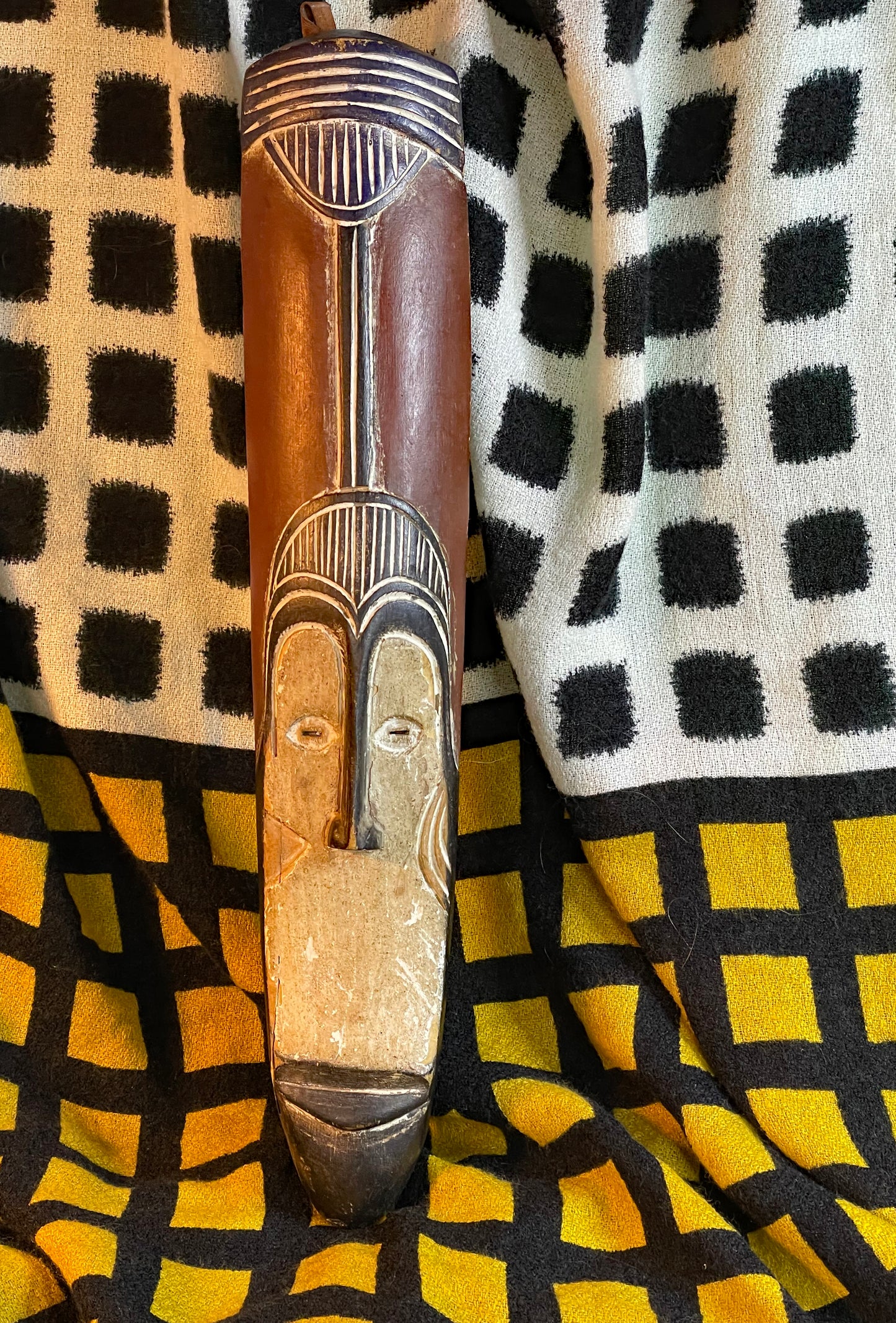 Elongated African tribal mask, full-length front view on patterned textile