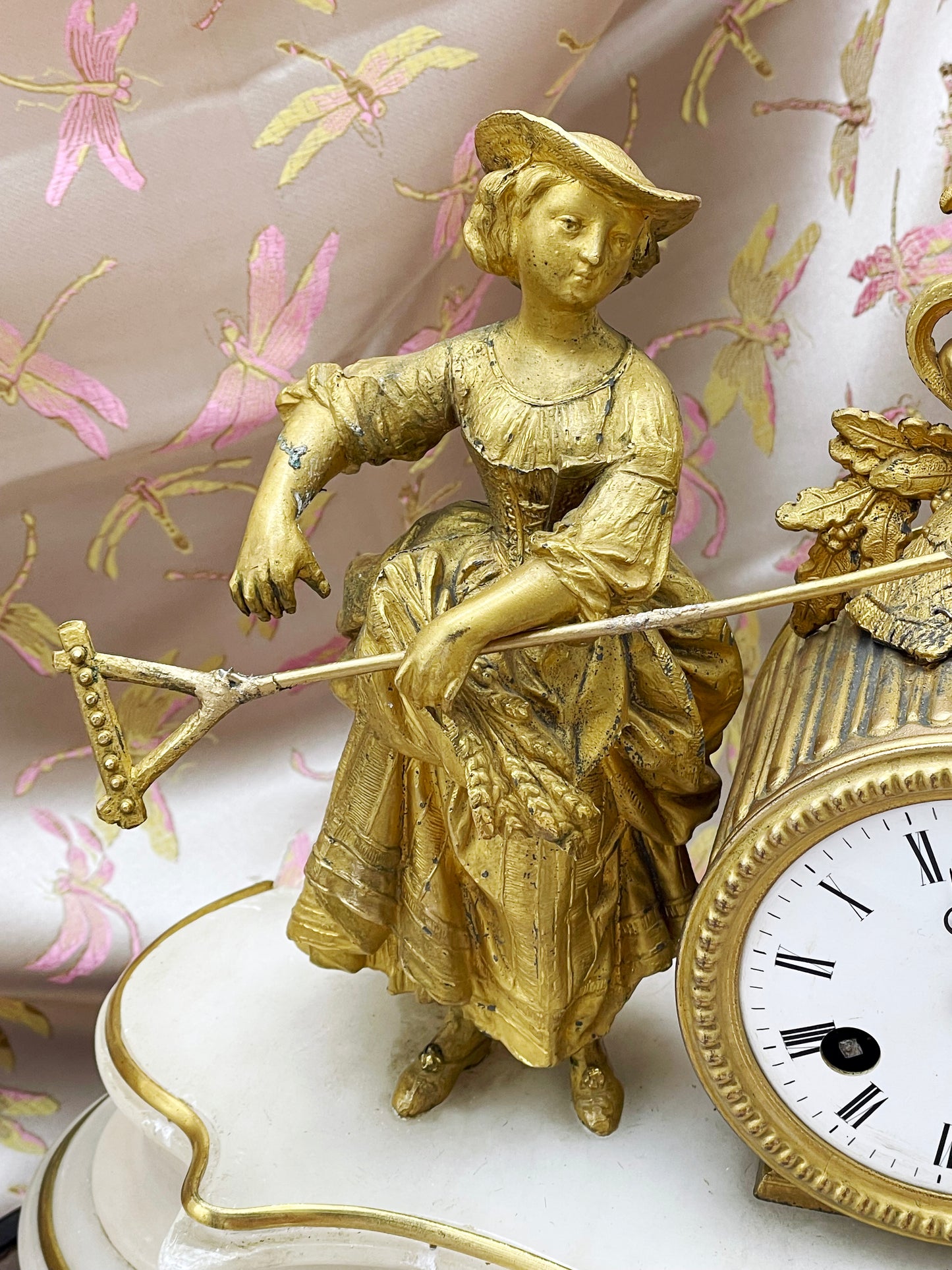 Gilt-bronze maiden leaning on her rake beside the white enamel Roman-numeral dial