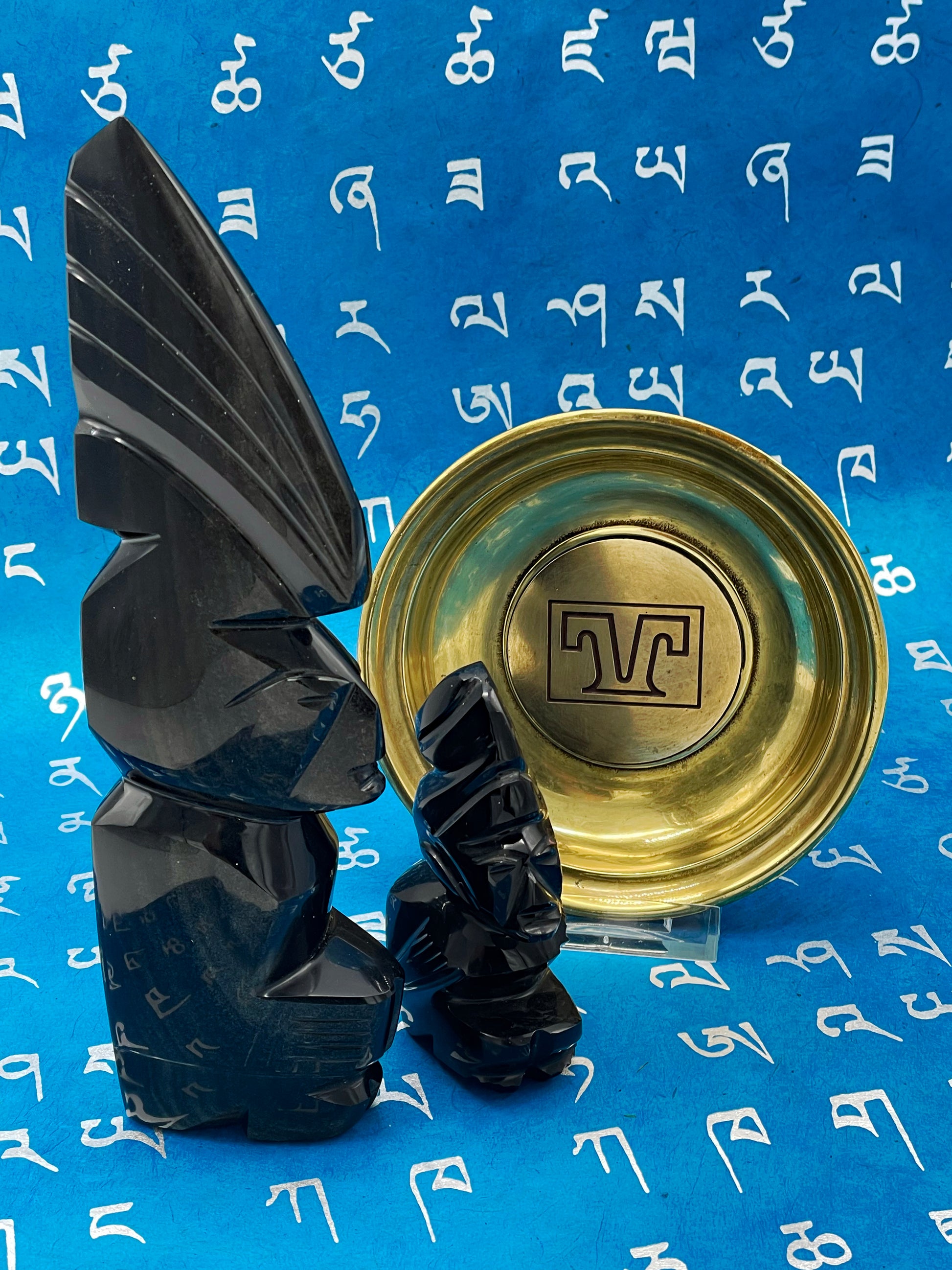Two carved black stone figures beside a solid brass engraved plate