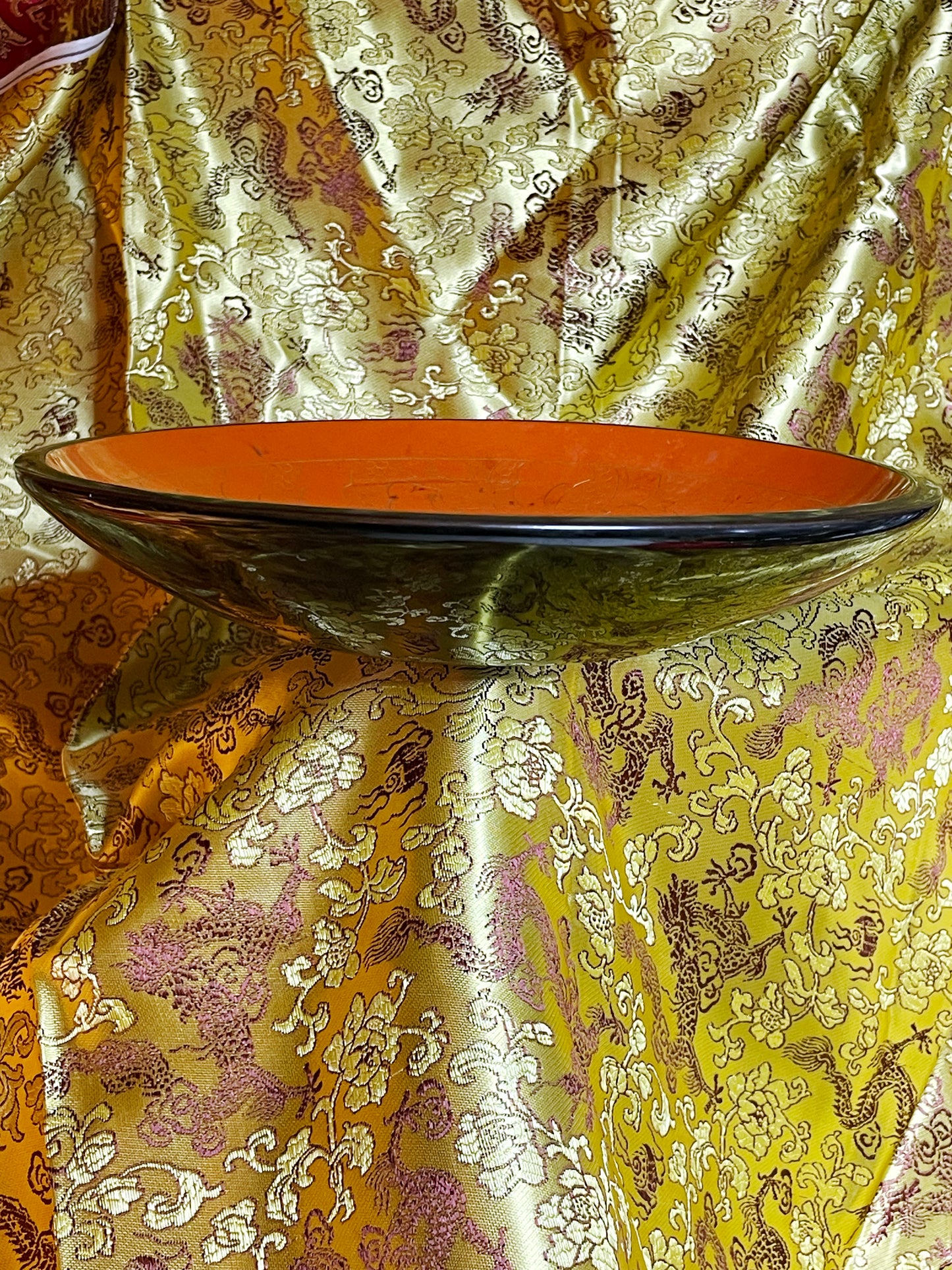 Three-quarter view of the lacquer plate on gold brocade showing orange interior and marbled black exterior