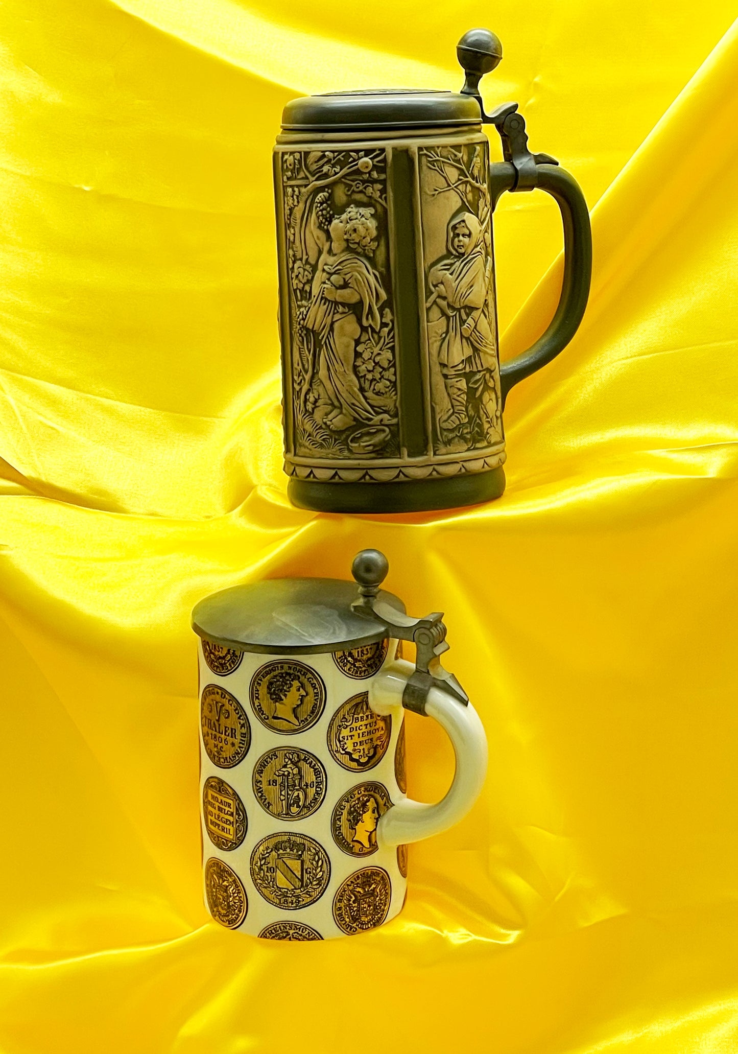 Two German Krüge with hinged pewter lids, relief stoneware stein above white Thaler coin stein