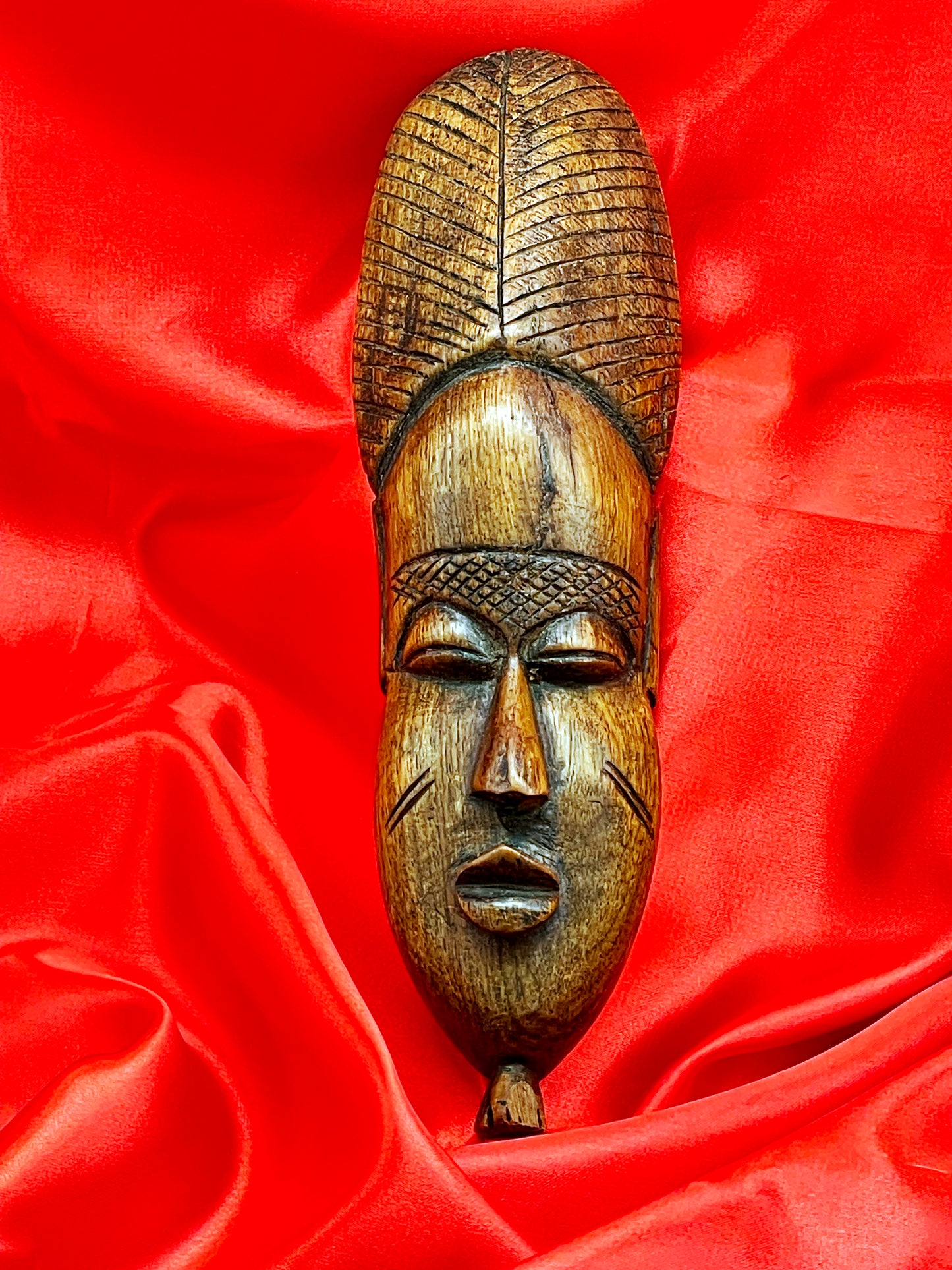 Front view of slender African Baule-style wood mask showing almond eyes and cheek scarification