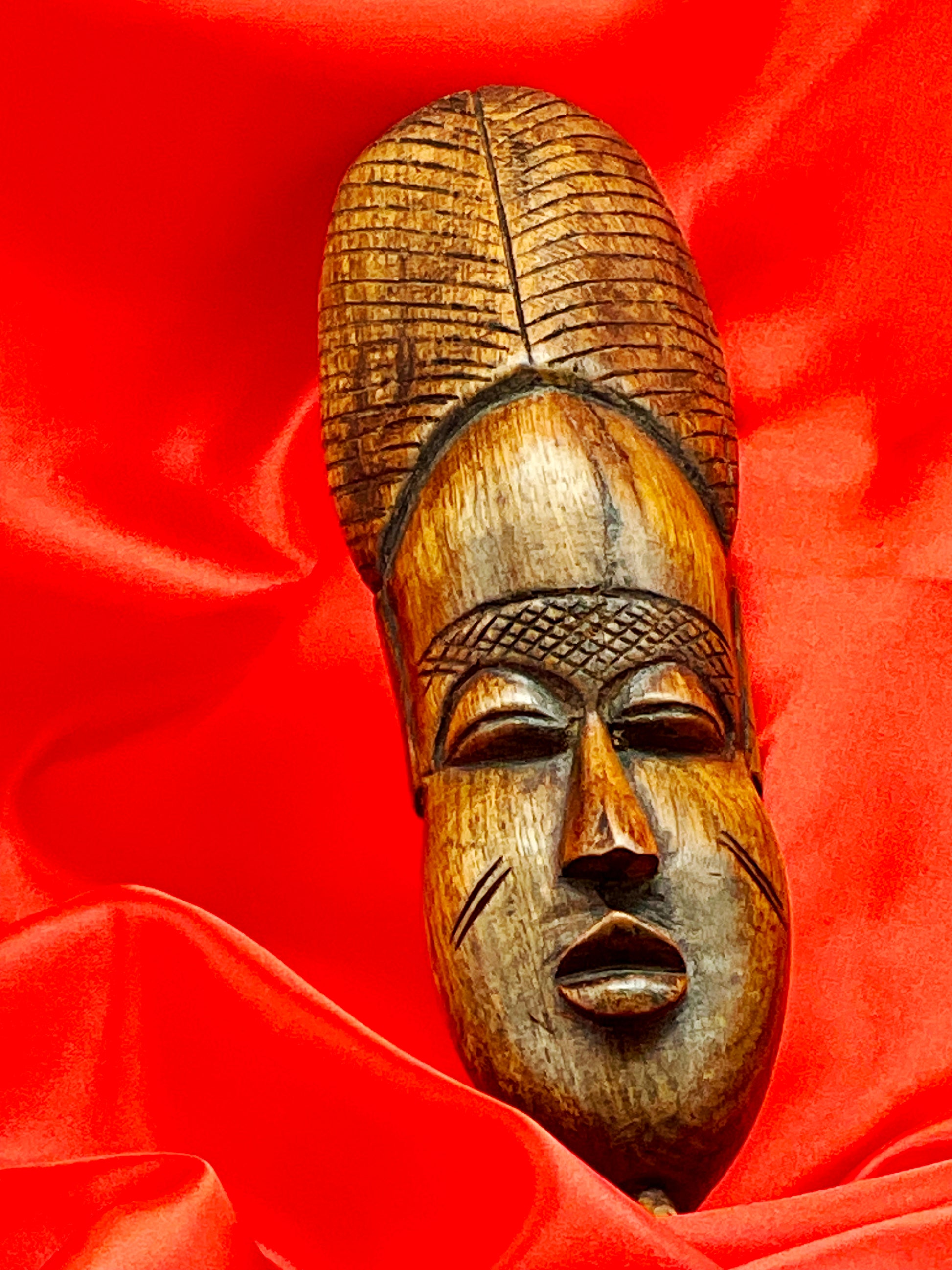Three-quarter angle of African carved wood mask revealing the relief of the face and crest