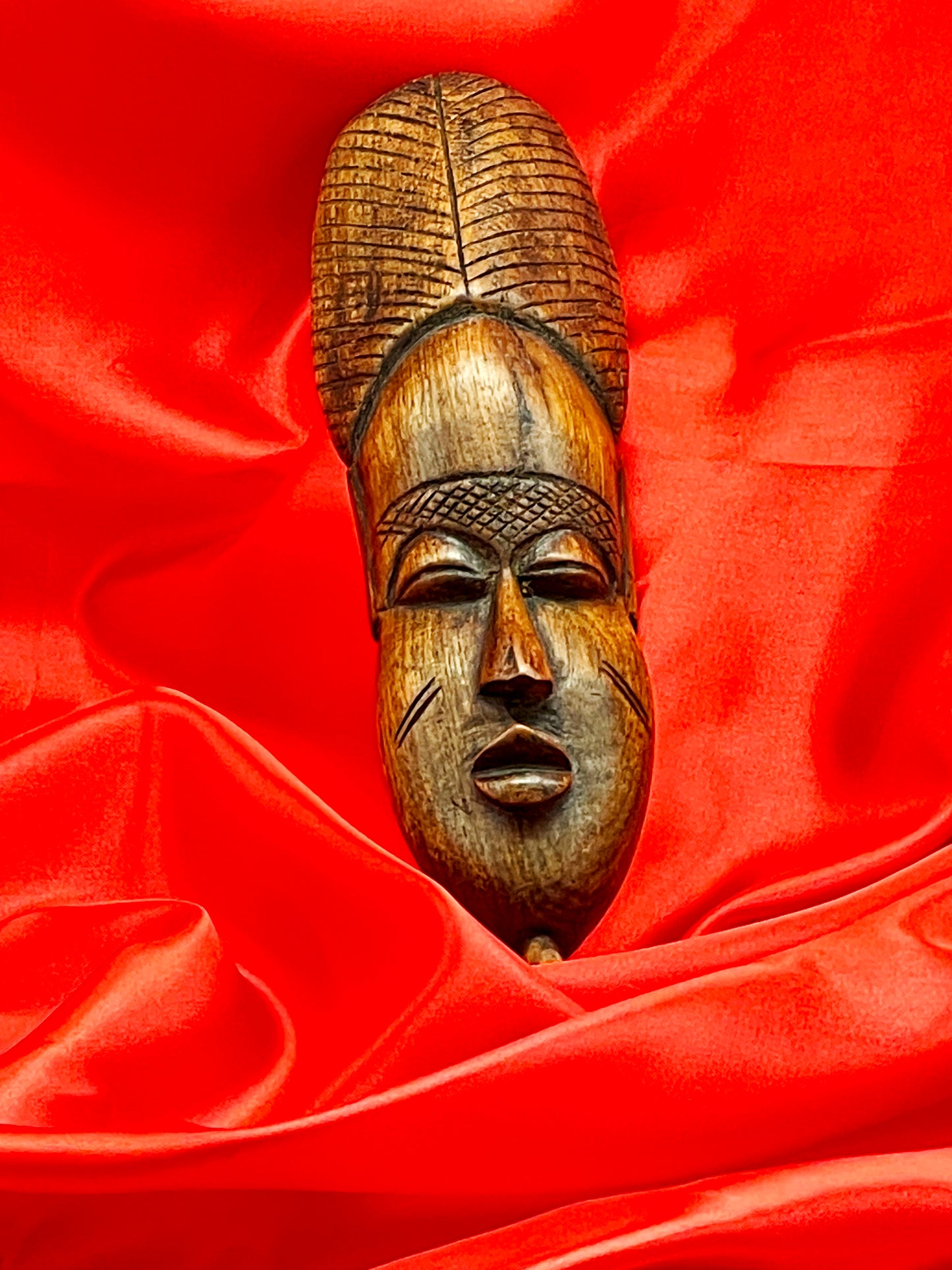 Warm-toned front view of carved African hardwood face mask wall hanging