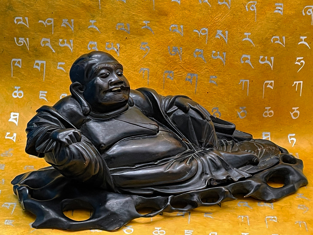 Antique ebony reclining laughing Buddha, three quarter view showing carved robe and platform